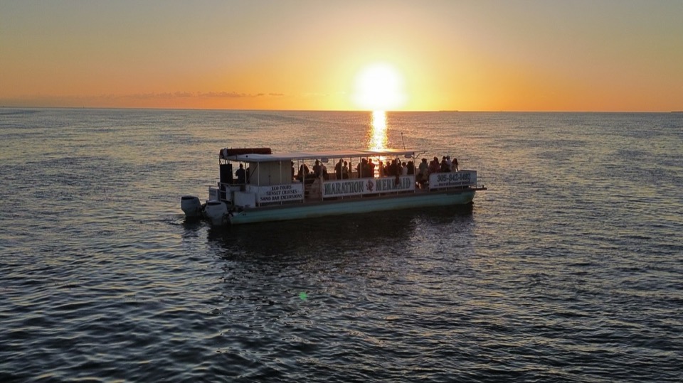 An aerial drone shot of the catamaran centered on the sun's reflection path across the water