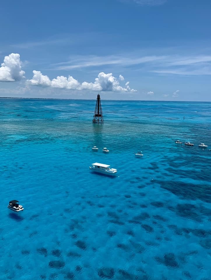 An aerial view of the Sombrero Reef lighthouse over clear blue reef water dotted with boats