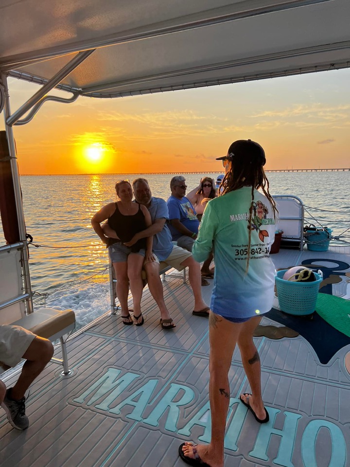 A crew member and guests on deck watching the golden sunset over the Seven Mile Bridge