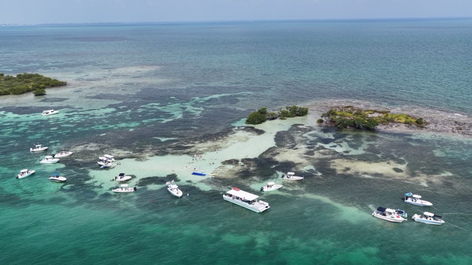 Aerial of the Marathon Mermaid and boats gathered at the turquoise Marathon sandbar beside a mangrove island