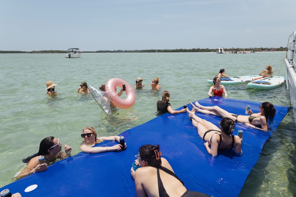 Guests relaxing on floating water mats and tubes in the shallow turquoise sandbar water