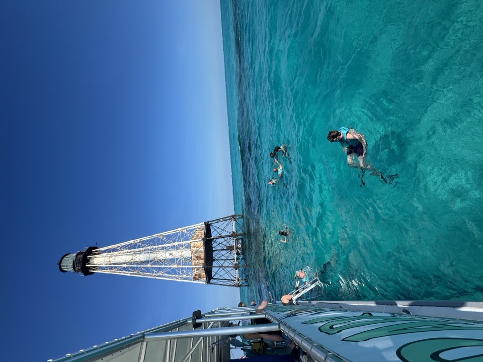 The Morada Mermaid catamaran and snorkelers beside a reef lighthouse in brilliant clear turquoise water