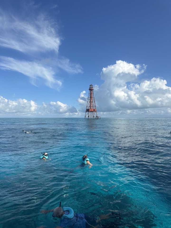 Snorkelers near a reef lighthouse under dramatic clouds in stunning clear water
