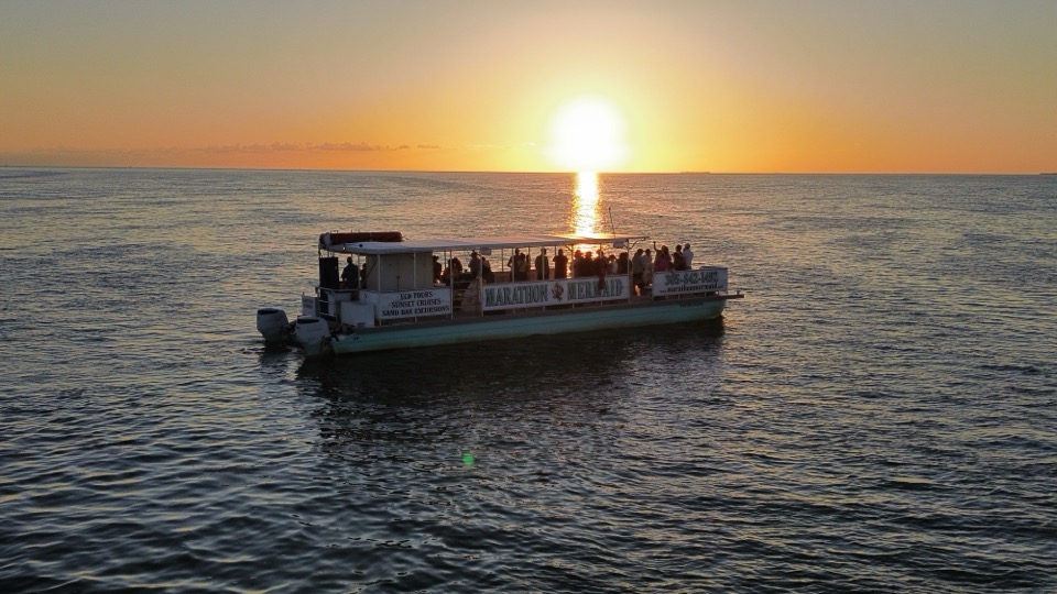 Aerial view of the Marathon Mermaid catamaran full of guests under a glowing low sun with its reflection streaking across the water