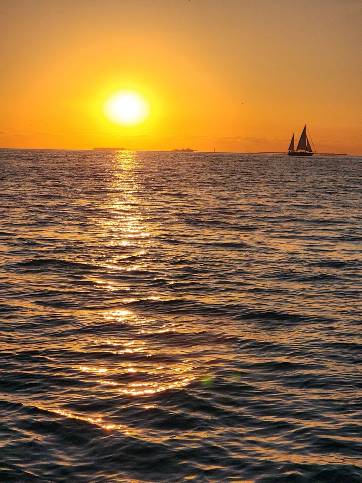A golden sunset with a distant sailboat silhouette and shimmering light trail on the water