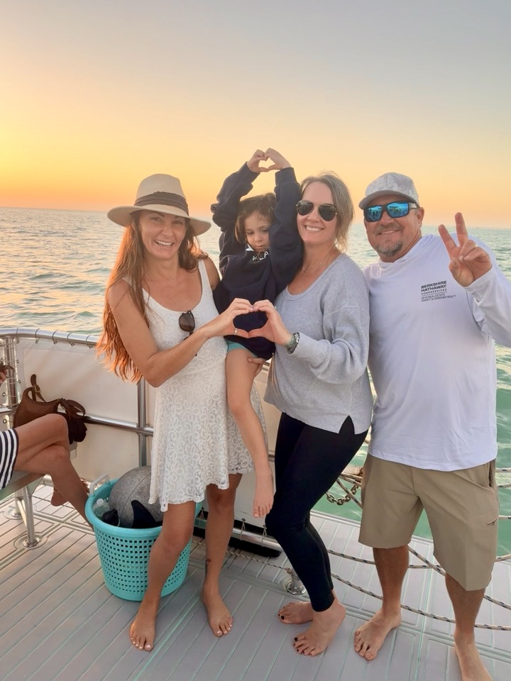 A family making heart shapes with their hands framing the setting sun on the deck at golden hour