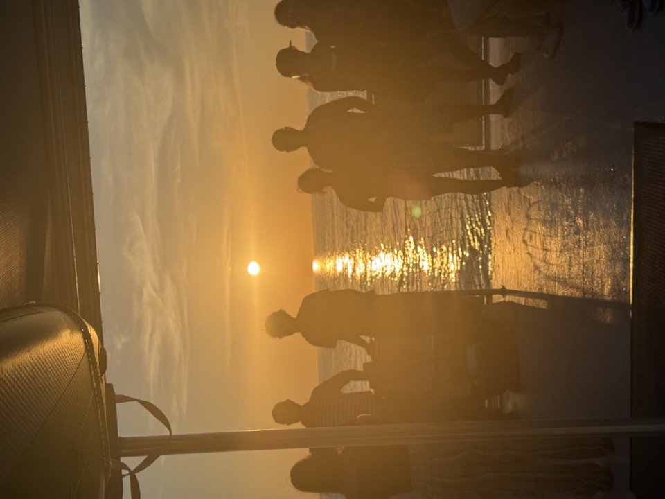 Guests silhouetted on deck against the golden reflection of the setting sun on the water