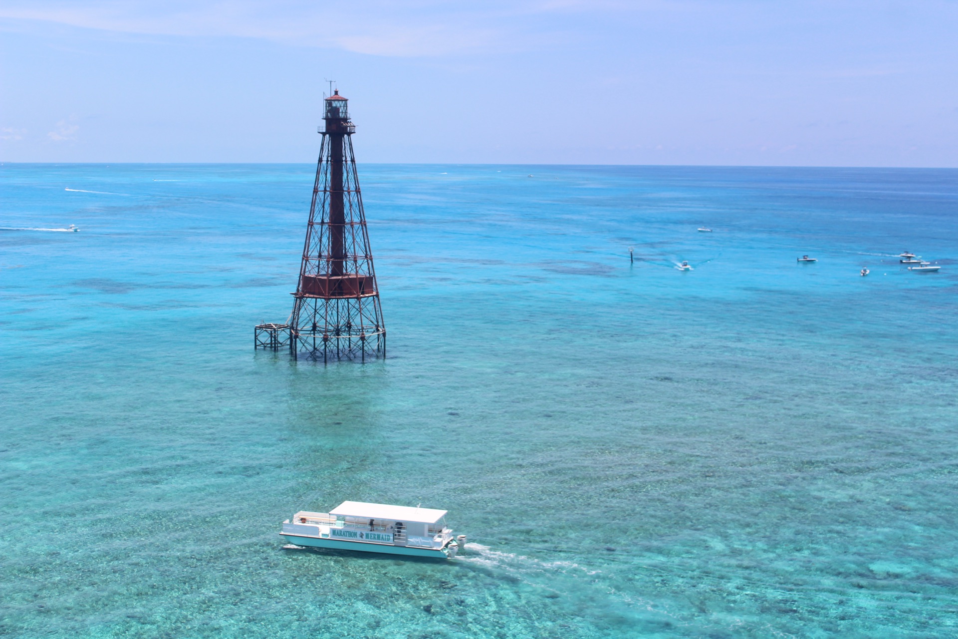 An aerial view of the catamaran cruising past a Keys reef lighthouse over vivid blue reef flats