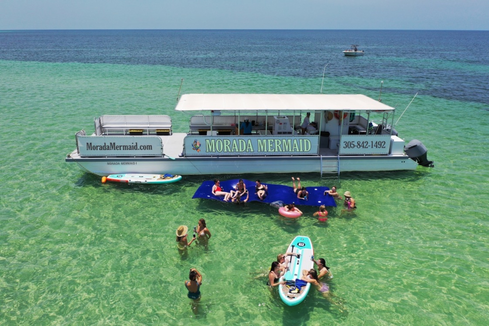 An aerial view of the Morada Mermaid catamaran over turquoise water with guests on floating mats and paddleboards