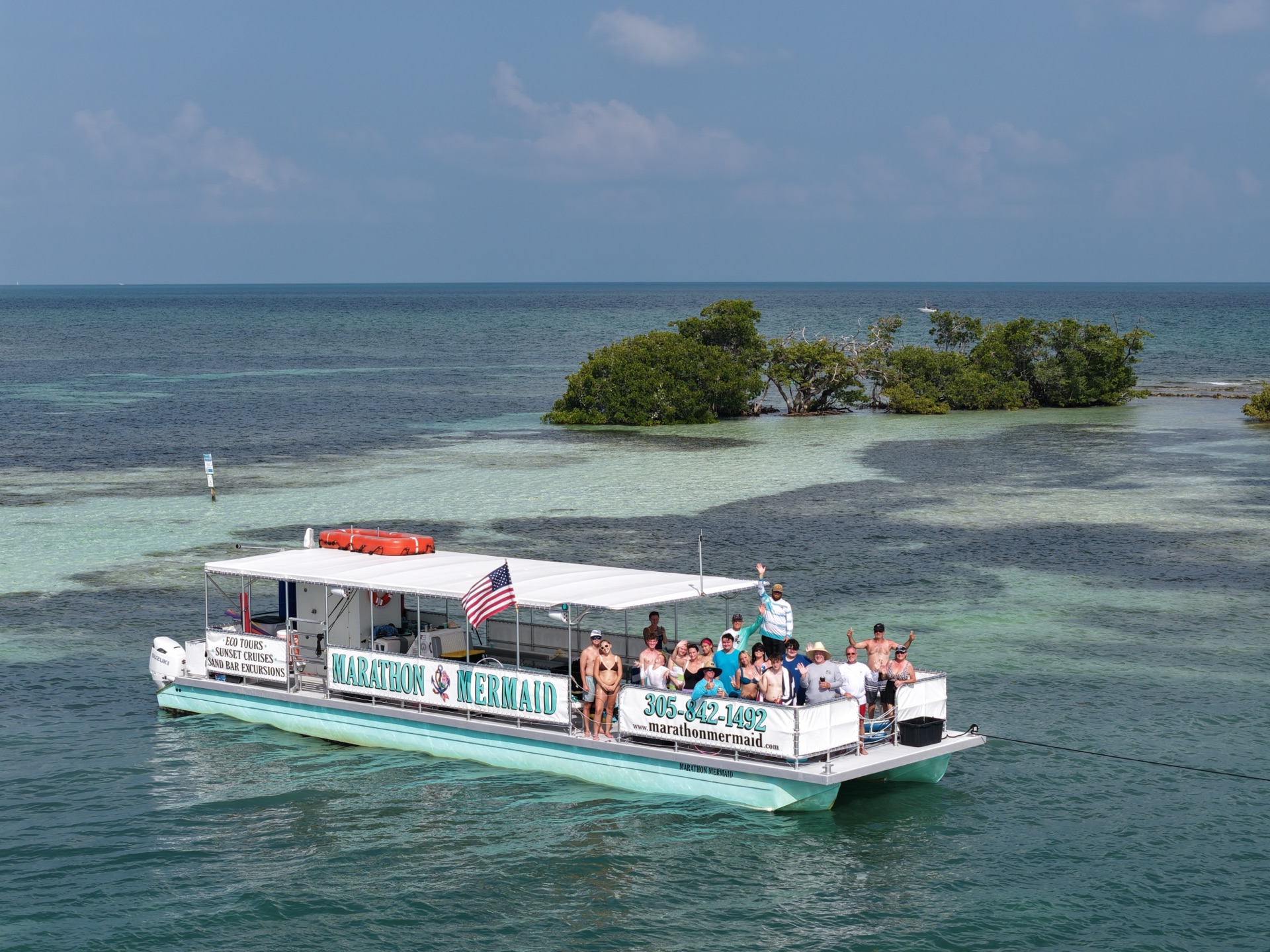 The Marathon Mermaid catamaran full of guests anchored at the turquoise Marathon sandbar by a mangrove island