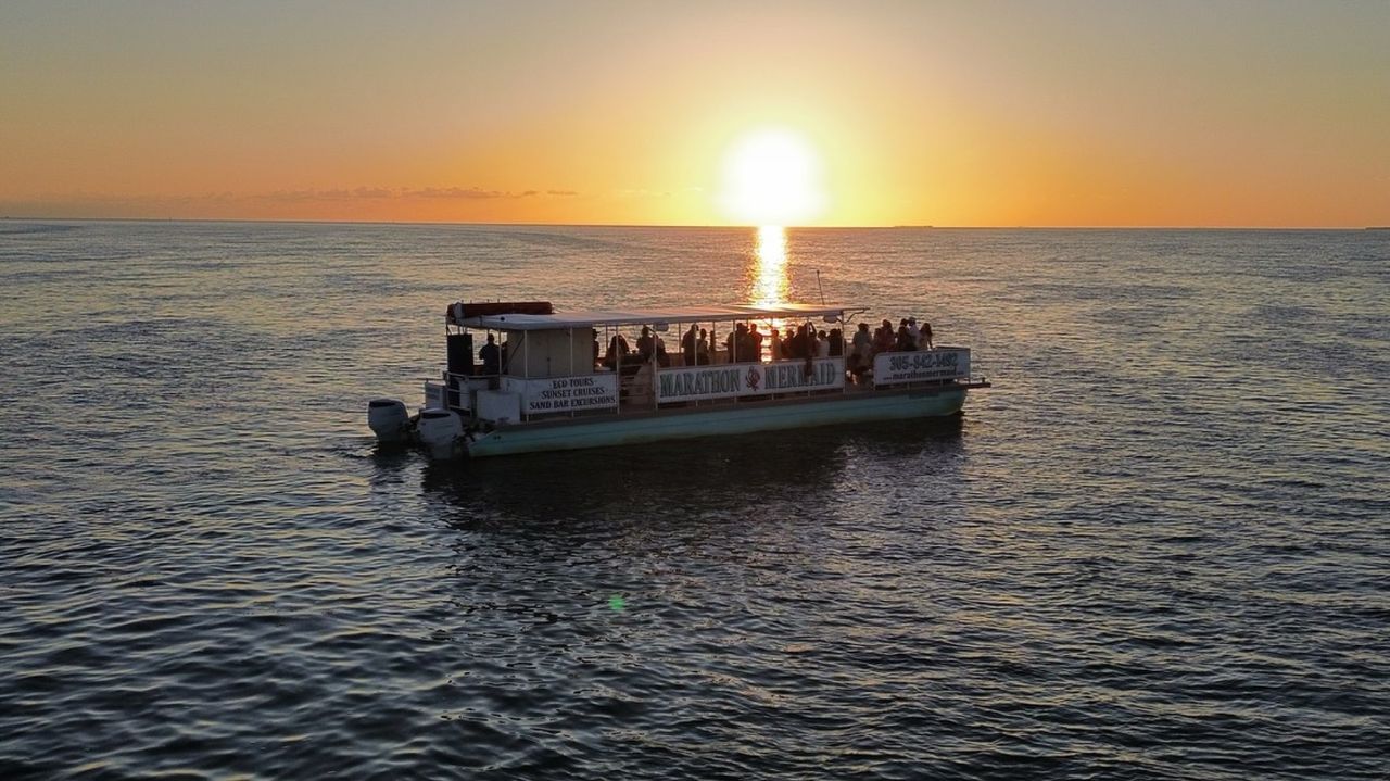 An aerial drone shot of the catamaran centered on the sun's reflection path across the water