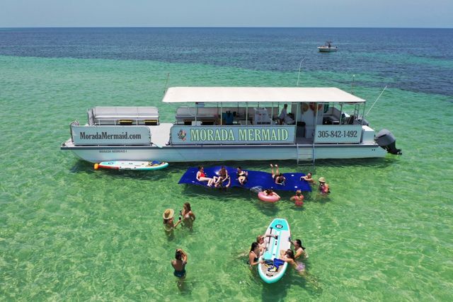 An aerial view of the branded Morada Mermaid at a sandbar with guests, floats and paddleboards