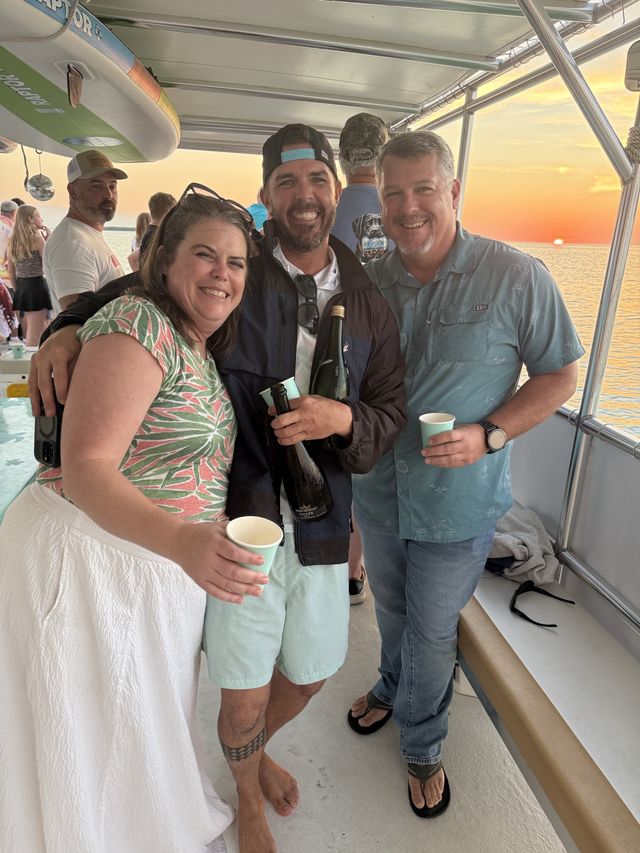 Three friends smiling with champagne as the sun sets behind them