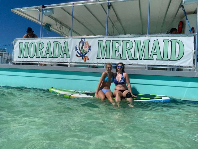 Two women on paddleboards beneath the Morada Mermaid banner