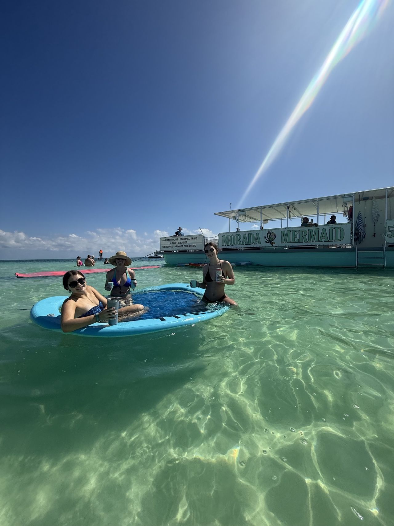 Guests on a paddleboard beside the Morada Mermaid in the clear sandbar shallows