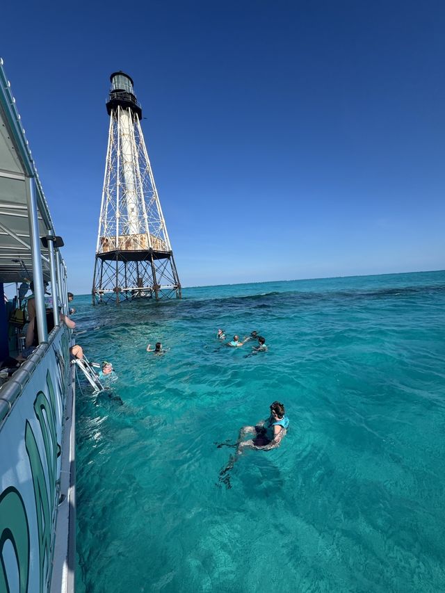The Morada Mermaid catamaran and snorkelers beside a reef lighthouse in brilliant clear turquoise water