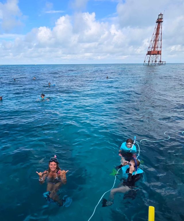 Snorkelers on a line at a reef lighthouse in deep blue water, one throwing a shaka