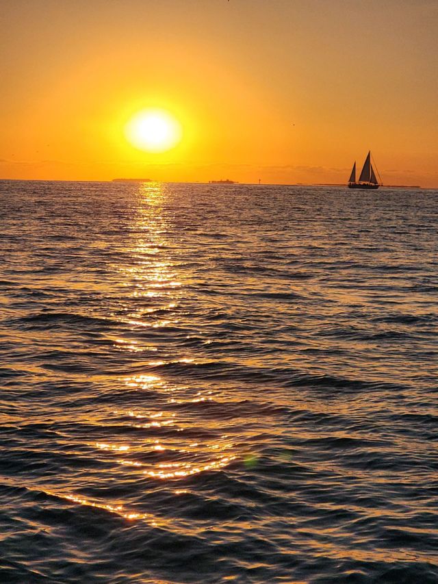 A golden sunset with a distant sailboat silhouette and shimmering light trail on the water