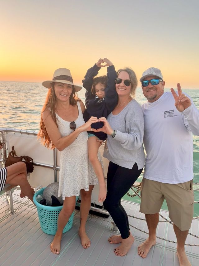 A family making heart shapes with their hands framing the setting sun on the deck at golden hour