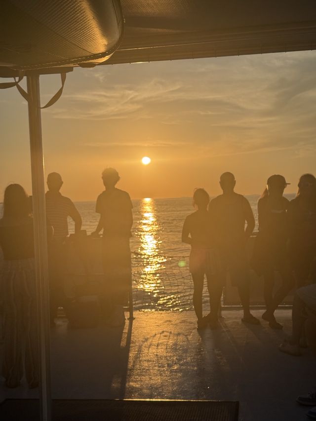 Guests silhouetted on deck against the golden reflection of the setting sun on the water